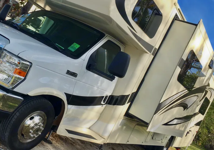 A white Ford E-Series Class C RV rental, a motorhome with an extended slide-out, is parked outdoors.. Jayco Greyhawk 2016