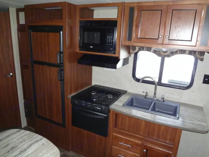 RV rental kitchen interior: wood cabinets, refrigerator, microwave, stove, double sink, and window.. Heartland Trail Runner 2017