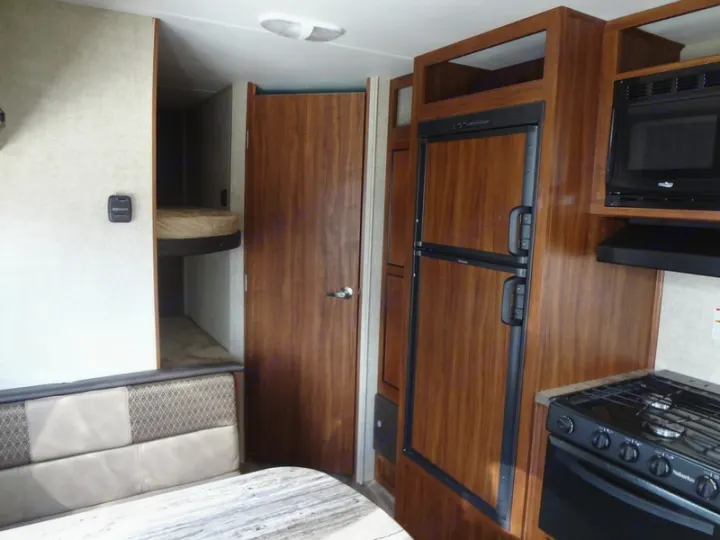 Interior of an RV rental showing kitchen with stove, microwave, fridge, dinette, and bunk beds. Perfect for family adventures!. Heartland Trail Runner 2017