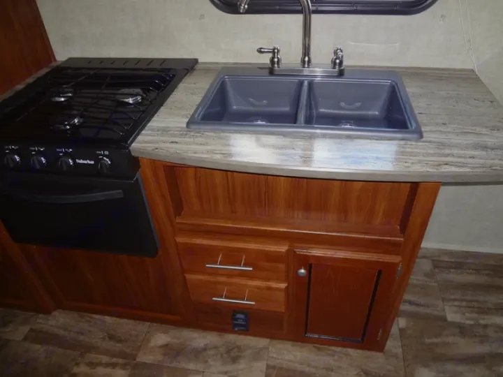 Modern RV rental kitchen with a black Suburban stove/oven, double sink, and wood cabinets. Perfect for your road trip cooking.. Heartland Trail Runner 2017