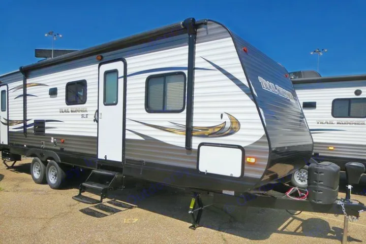 A shiny white and dark gray travel trailer, ideal for an RV rental adventure, parked under a clear sky. It features an awning & multiple windows.. Heartland Trail Runner 2016