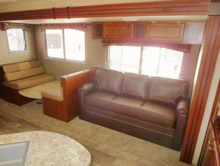 RV rental's spacious interior: brown sofa, dinette, and bright windows, offering a comfortable living area.. Heartland Trail Runner 2016