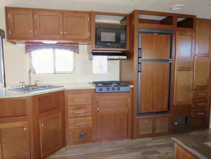 RV rental kitchen: wood cabinets, dual sink, microwave, stove, large fridge, and ample storage, perfect for your next adventure.. Heartland Trail Runner 2016