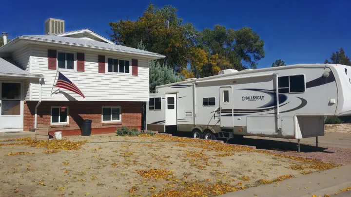 Challenger fifth-wheel RV rental parked by a home with fall leaves and a US flag, ready for adventure.. Keystone Challenger 2005