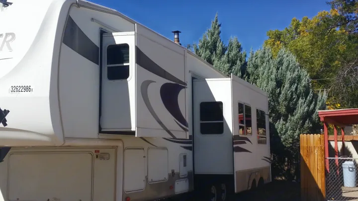 White fifth-wheel RV rental with slide-outs open, parked on a sunny day surrounded by trees.. Keystone Challenger 2005