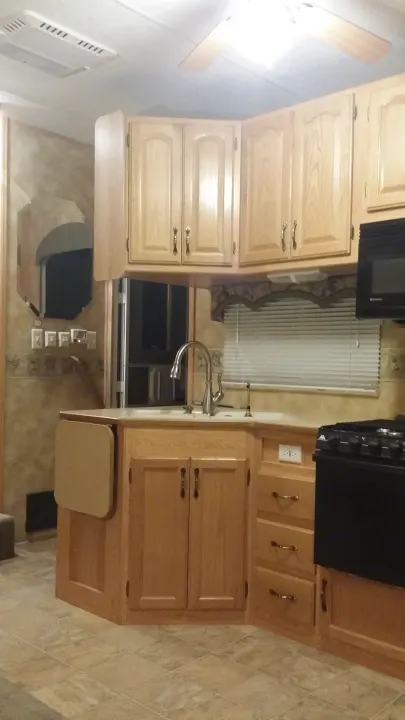 This RV rental's kitchen features light wood cabinets, a sink, microwave, stove, AC, and a ceiling fan.. Keystone Challenger 2005
