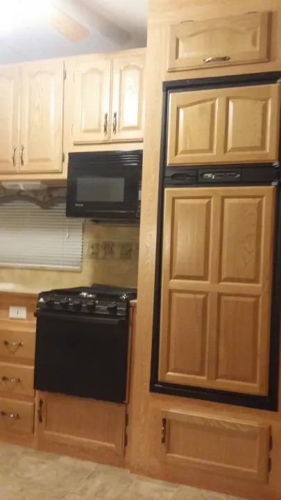 RV rental kitchen featuring light wood cabinets, black microwave, stove, and refrigerator with wood panel doors.. Keystone Challenger 2005