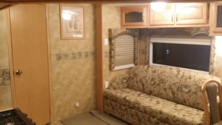 RV rental: View of an RV's living area with a floral sofa, wooden cabinets, blinds on windows, and a light-colored door.. Keystone Challenger 2005