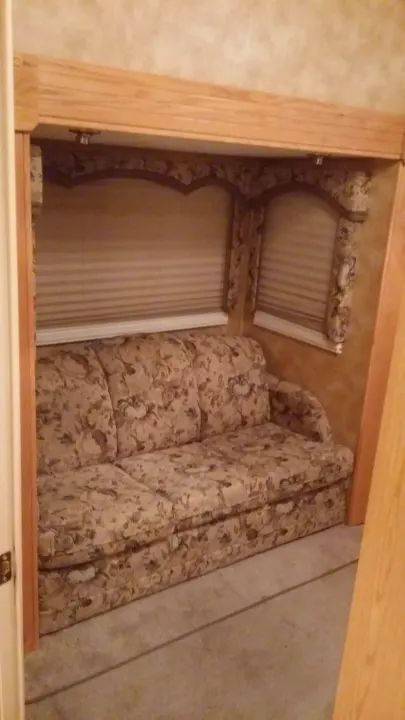 Floral sofa in a cozy, built-in nook with blinds, offering comfortable seating in this RV rental. Ideal for relaxing.. Keystone Challenger 2005