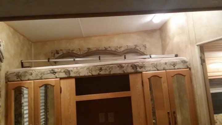 Inside an RV rental: a comfortable bunk bed with a safety rail over wooden storage cabinets and media space.. Keystone Challenger 2005