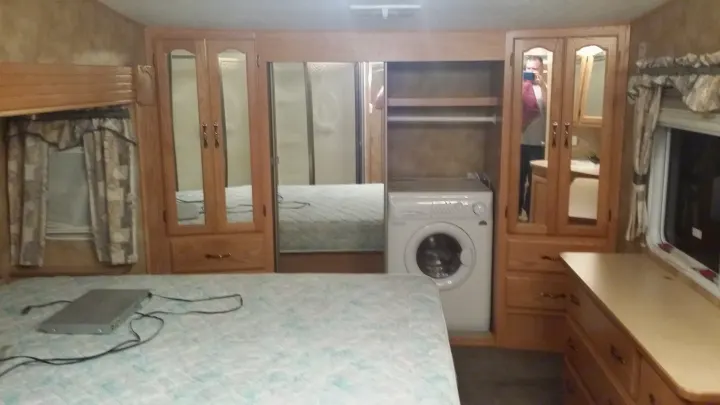 Explore this RV rental's bedroom, featuring a comfy bed, wood cabinetry, and a convenient built-in washing machine.. Keystone Challenger 2005
