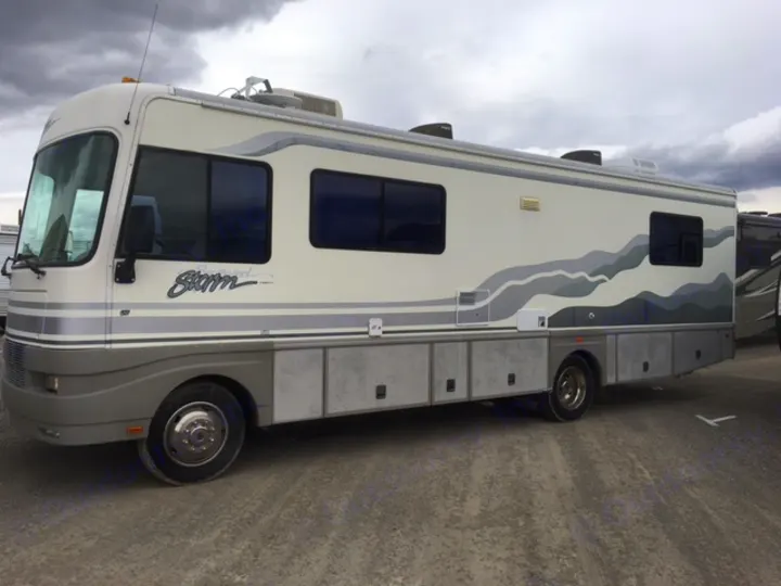 A cream & grey Storm RV, perfect for your next RV rental adventure, sits on a gravel lot under a cloudy sky.. Fleetwood Other 2000
