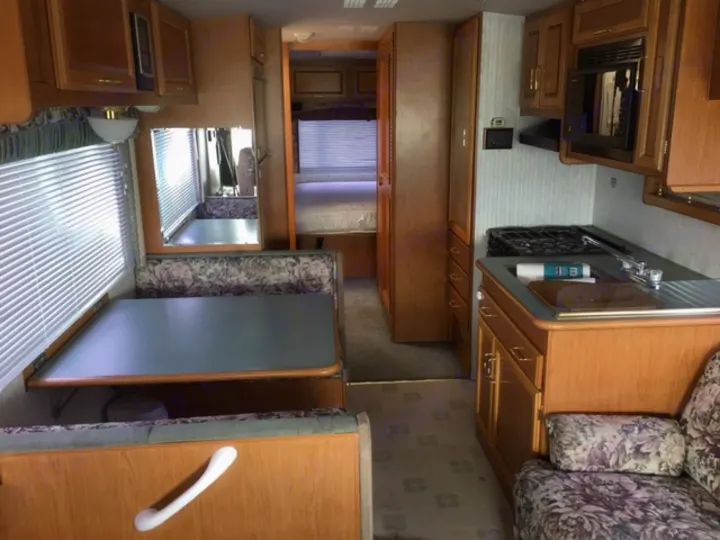 Interior view of an RV rental: kitchen with stove & sink, dinette with table, and a hallway to the bedroom.. Fleetwood Other 2000