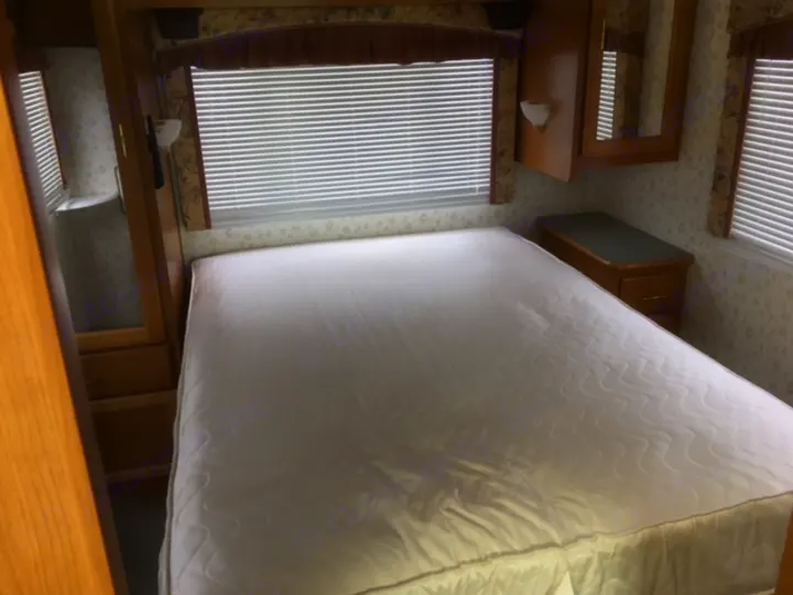 Inside an RV rental: a compact bedroom with a white mattress, windows, and wood cabinetry.. Fleetwood Other 2000