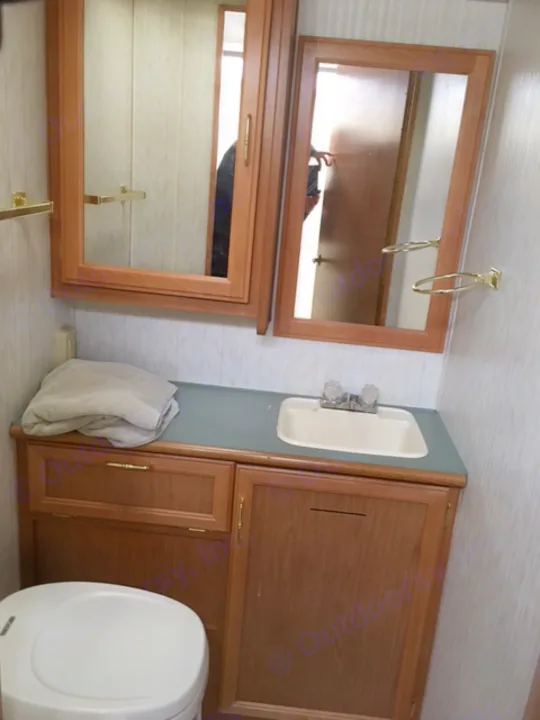 Interior view of an RV rental bathroom, featuring a sink, toilet, and wooden cabinets with mirrors. Compact and functional design.. Fleetwood Other 2000