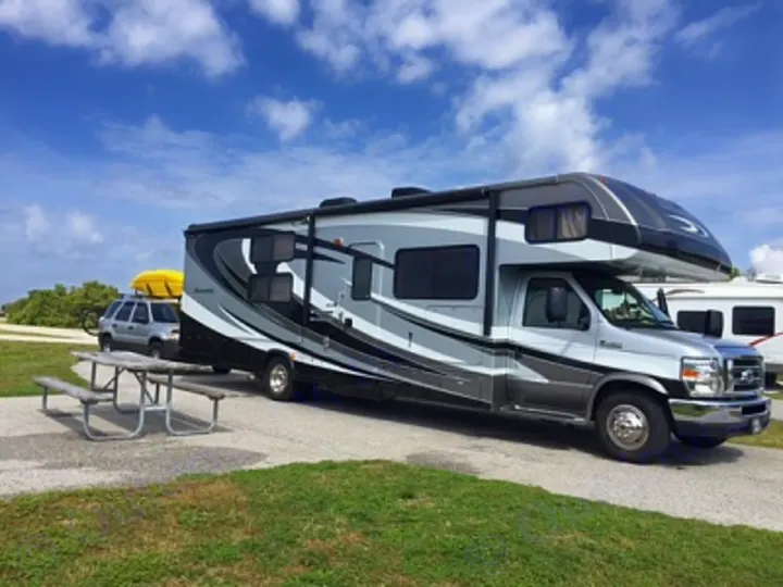 Modern gray RV rental parked at a sunny campsite, towing an SUV with kayaks for your next adventure.. Forest River Sunseeker LE 2015