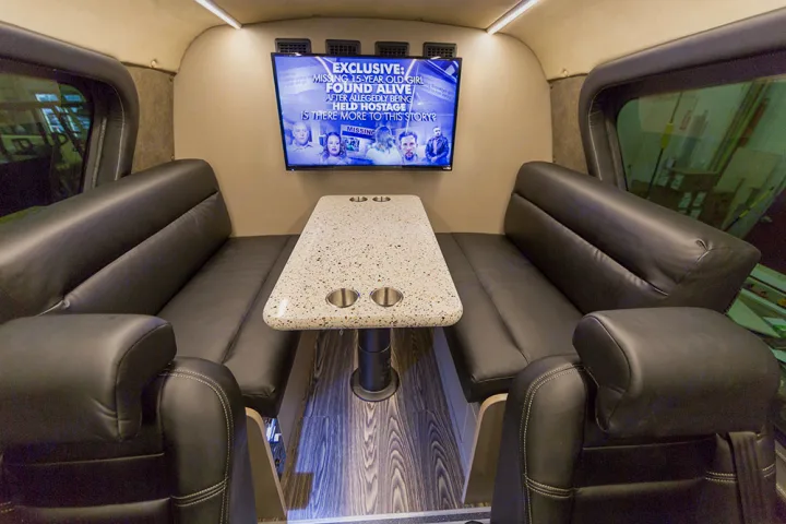 Spacious RV rental interior featuring plush black leather seating, a central table with cupholders, and a TV.. Custom Coach Mauck2 2015
