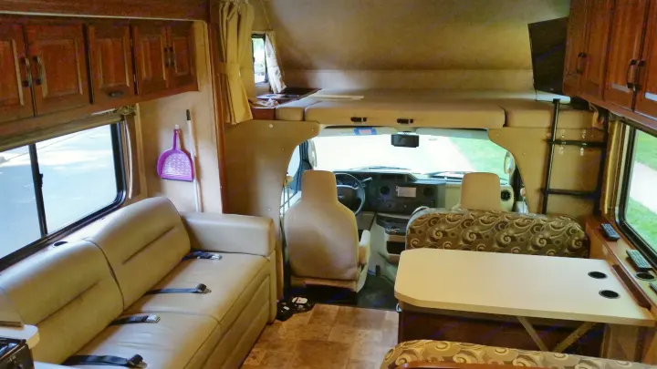 Interior of an RV rental: driver's area, over-cab bunk bed, sofa, and dining table, all set for travel comfort.. Forest River Sunseeker LE 2015
