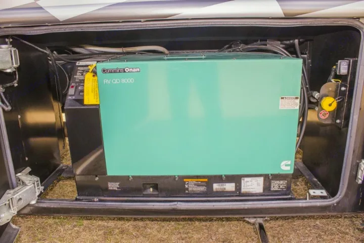 Inside an RV compartment, a teal green Cummins Onan RV QD 8000 generator, providing essential power for your rv rental.. Dynamax Corp Grand Sport 2015