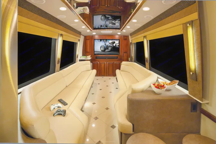 Spacious luxury RV rental interior: opposing beige leather sofas, dual TVs (gaming/racing), and snacks.. Dynamax Corp Grand Sport 2015