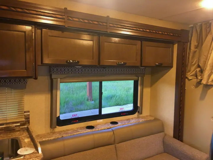 RV rental interior: rich wood cabinets, wide window with 'EXIT' signs, comfortable sofa, and countertop with sink area. Perfect for travel.. Other Other 2018