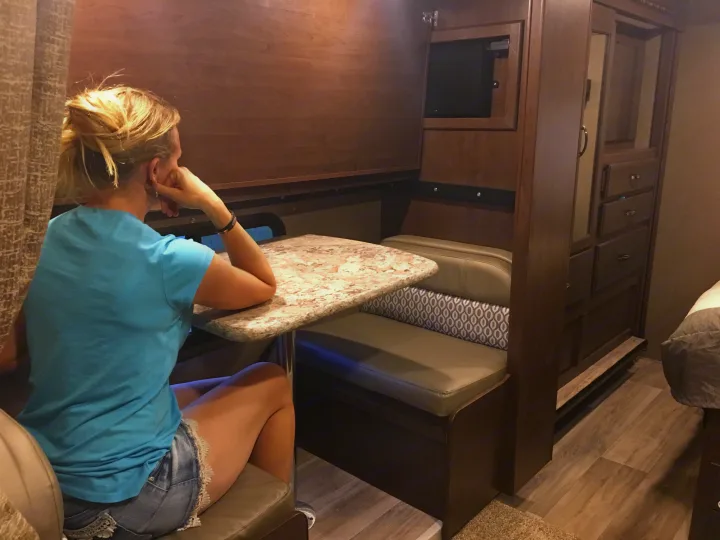 RV rental interior: woman relaxes at dinette table. Features cozy seating, built-in TV, and wood-toned cabinetry.. Other Other 2018