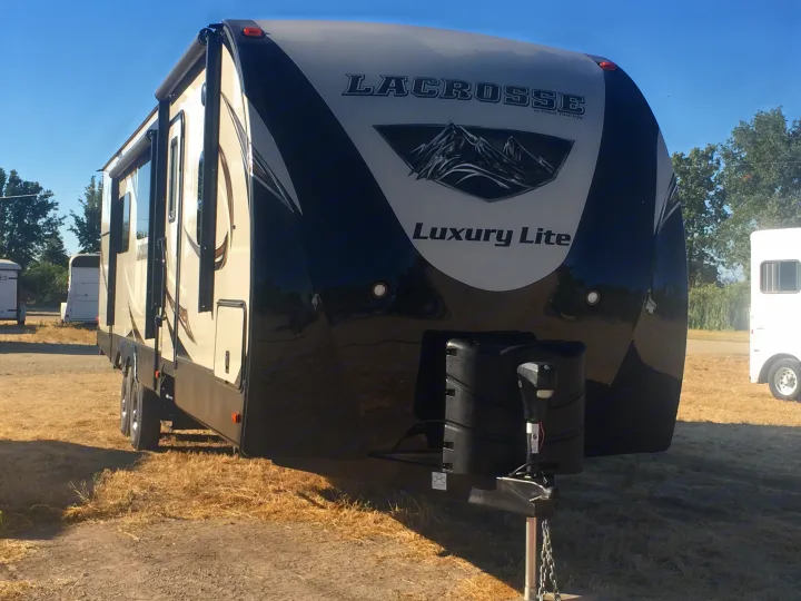Front of a modern black and tan LaCrosse Luxury Lite travel trailer, a great RV rental option, parked on a dry lot.. Prime Time Lacrosse 2017