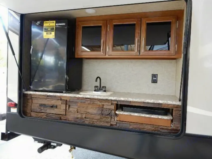 RV rental: Outdoor kitchen with black fridge, sink, wood cabinets, and a pull-out storage drawer, set in stone-look base.. Prime Time Lacrosse 2017