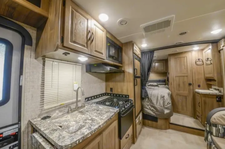 Spacious RV rental interior: well-equipped kitchen with stove, sink, and microwave, plus a cozy bedroom area.. Coachmen Prism 2150 2018
