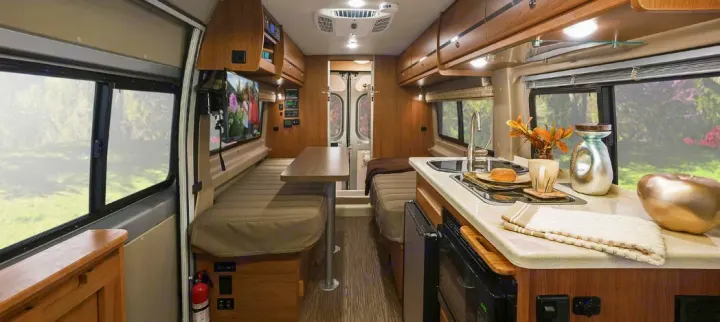 Spacious RV rental interior. View the kitchen with sink/stove, dining area, lounge with TV, and rear beds in this modern camper van.. Winnebago Travato 2018