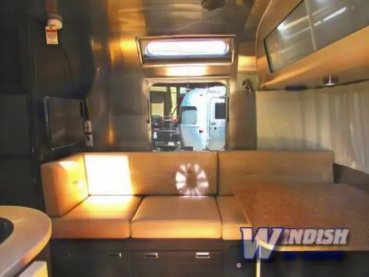 RV rental interior: long tan sofa, dining table, mounted TV, and polished aluminum walls for a spacious lounge.. Airstream International Signature 25 2018