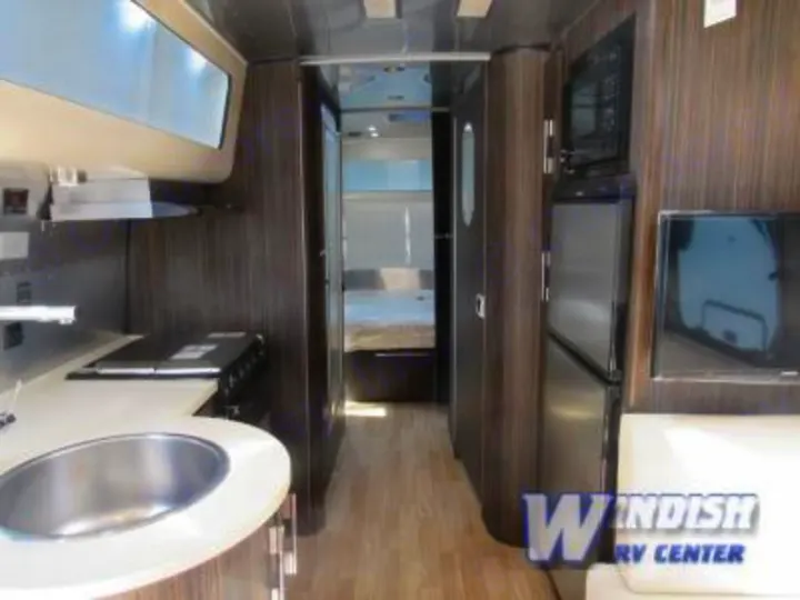 Spacious RV rental interior featuring a galley kitchen, living area with TV and fridge, leading to a rear bedroom.. Airstream International Signature 25 2018