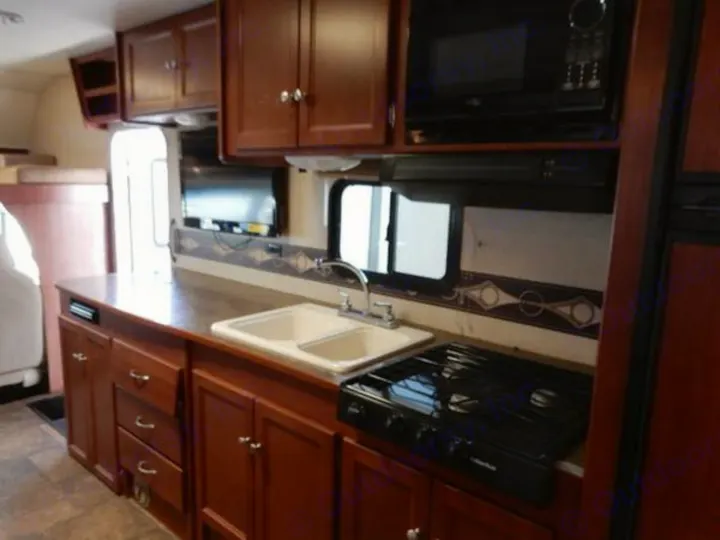 An RV rental kitchen showcasing dark wood cabinets, a double sink, stovetop, and microwave, ready for your adventures.. Winnebago ITASCA 2014