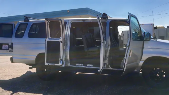 Custom silver Ford RV rental van with all doors open, showing spacious interior and roof rack for adventure.. Ford E-350 2009