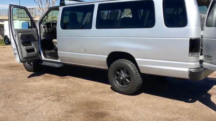 Spacious silver Ford E-350 van with open doors, rugged tires, and roof rack. Perfect for your next rv rental adventure.. Ford E-350 2009