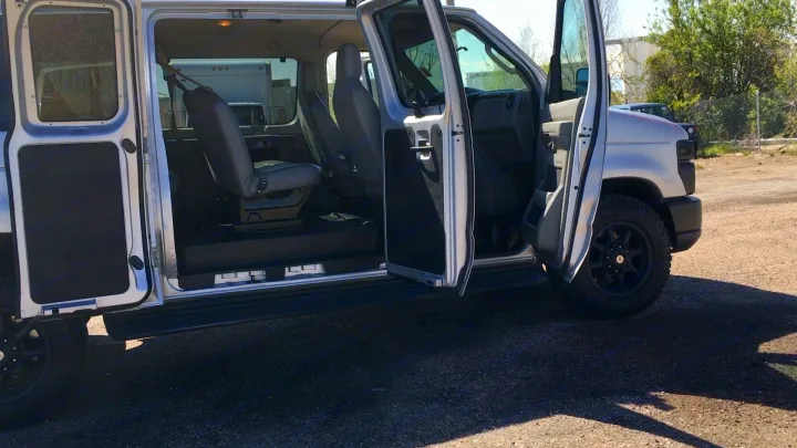 This silver custom van, perfect for an RV rental, shows its open doors, spacious interior, and rugged tires.. Ford E-350 2009