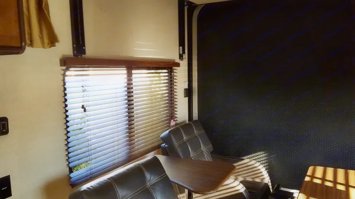 Sun-drenched RV rental interior. Light streams through window blinds, illuminating dark chairs and a side table.. Forest River Salem Cruise Lite 2017