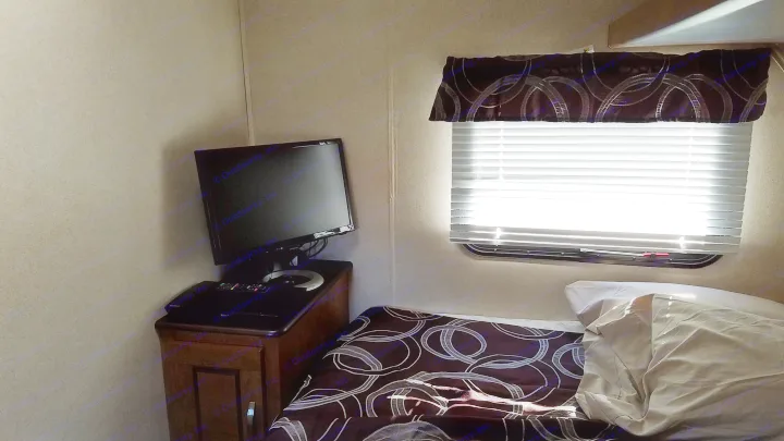 Cozy RV rental bedroom with a TV on a nightstand, patterned bed, and bright sunbeams through the window blinds.. Forest River Salem Cruise Lite 2017