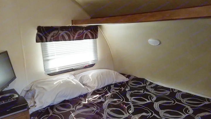 Inside a cozy RV rental bedroom. Features include a bed, pillows, window with blinds, and a TV. Sunlight illuminates the space.. Forest River Salem Cruise Lite 2017