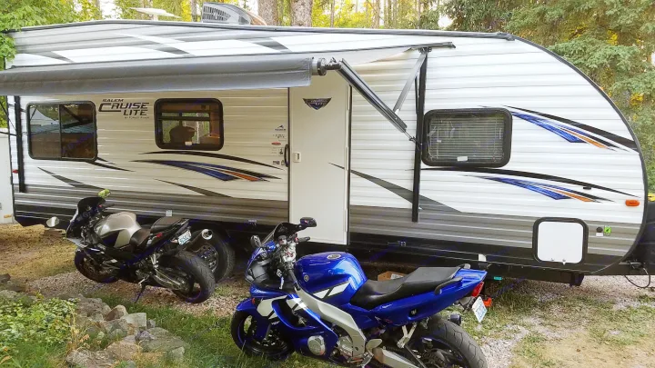 RV rental travel trailer with awning out, two motorcycles parked on a gravel pad.. Forest River Salem Cruise Lite 2017