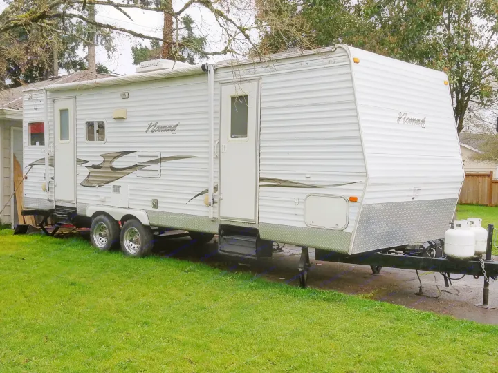 White Nomad travel trailer with an awning, ready for your next rv rental adventure. Features include multiple windows and propane tanks.. Skyline Nomad 2006