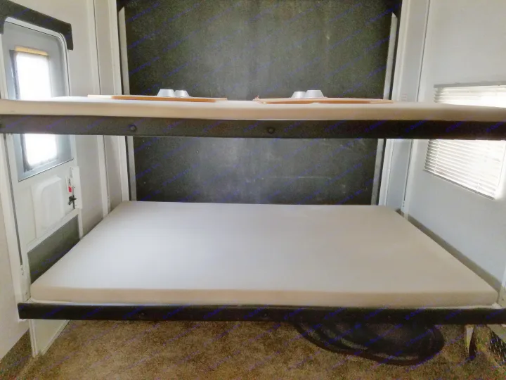 An RV rental's sleeping area with sturdy upper and lower bunk beds, complete with mattresses. A door and window are seen.. Heartland Cyclone 2009