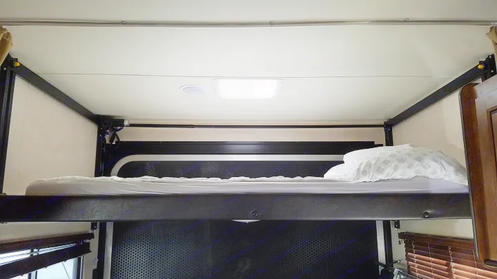 Looking up at a comfy RV rental upper bunk with light bedding, an overhead light, and a circular vent above.. Forest River Salem Cruise Lite 2017