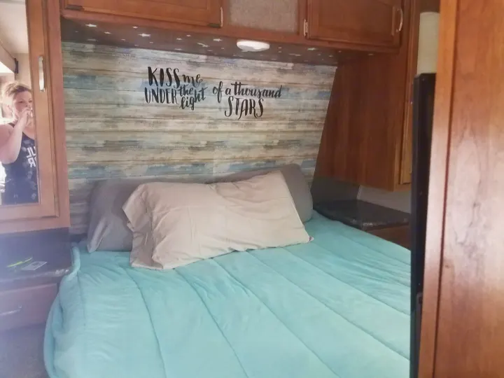 Cozy RV rental bedroom with unique "KISS me UNDER the light of a thousand STARS" headboard and soft blue bedding.. Keystone RV Springdale 2017