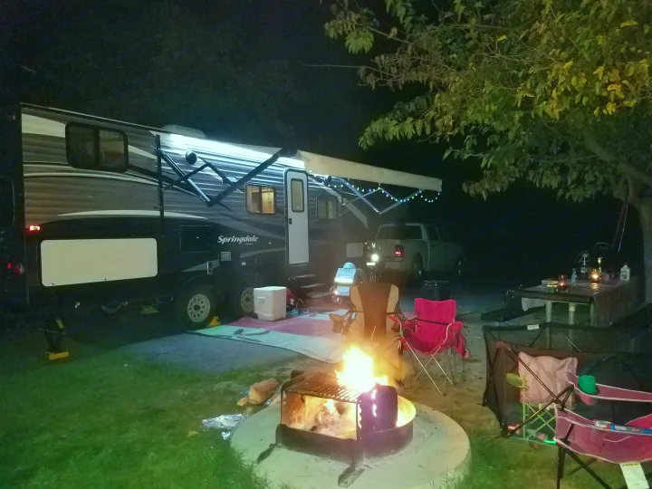 Nighttime RV rental camping: a bright Springdale travel trailer, a warm campfire, and outdoor seating under trees.. Keystone RV Springdale 2017