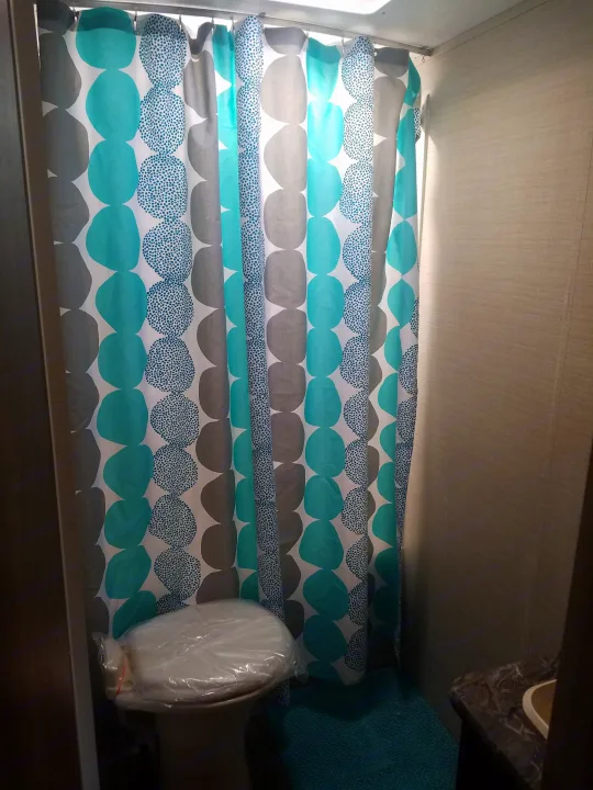 Clean and compact RV rental bathroom featuring a modern teal shower curtain, a protected toilet, and small vanity.. Keystone RV Springdale 2017