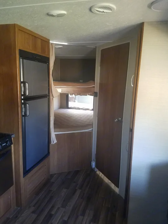 Inside this RV rental: compact kitchen with fridge and cozy bunk beds. A functional space for family travel.. Keystone RV Springdale 2017