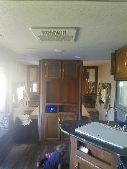 Cozy RV rental interior showing a kitchen sink, entertainment center, and bunk beds. A child on the floor suggests family travel.. Keystone RV Springdale 2017