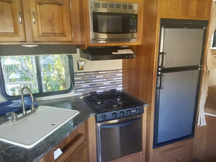 Well-equipped RV rental kitchen featuring a sink, microwave, stove/oven, refrigerator, and wooden cabinetry.. Keystone RV Springdale 2017