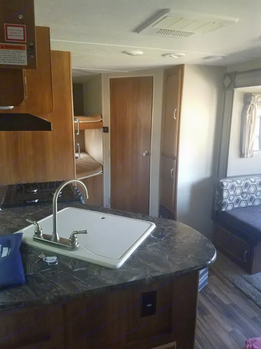 An RV rental's inviting interior, showcasing a kitchen with sink and stove, bunk beds, and a comfortable dinette.. Keystone RV Springdale 2017